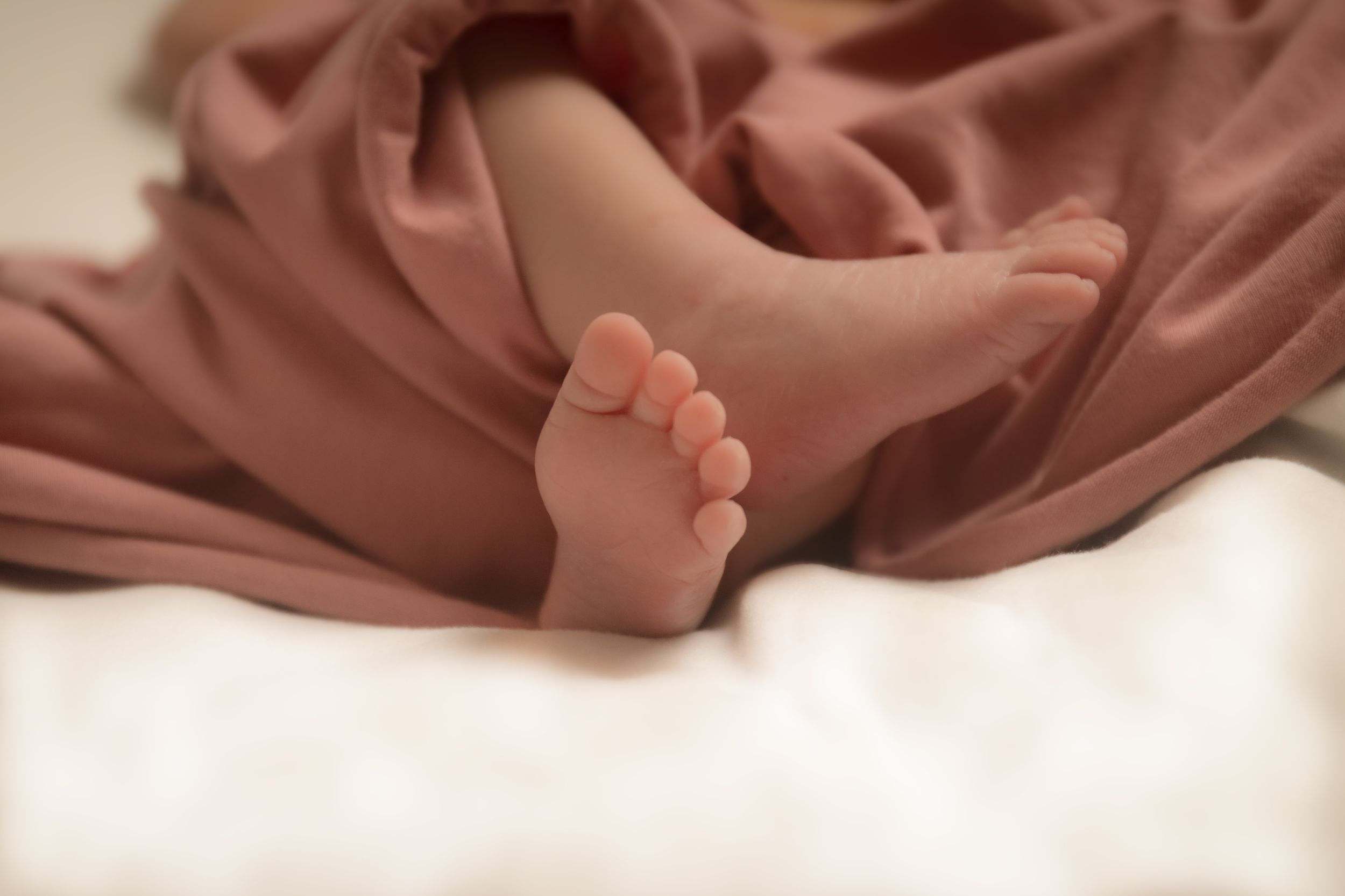 Newborn baby feet wrapped in a soft blush pink blanket