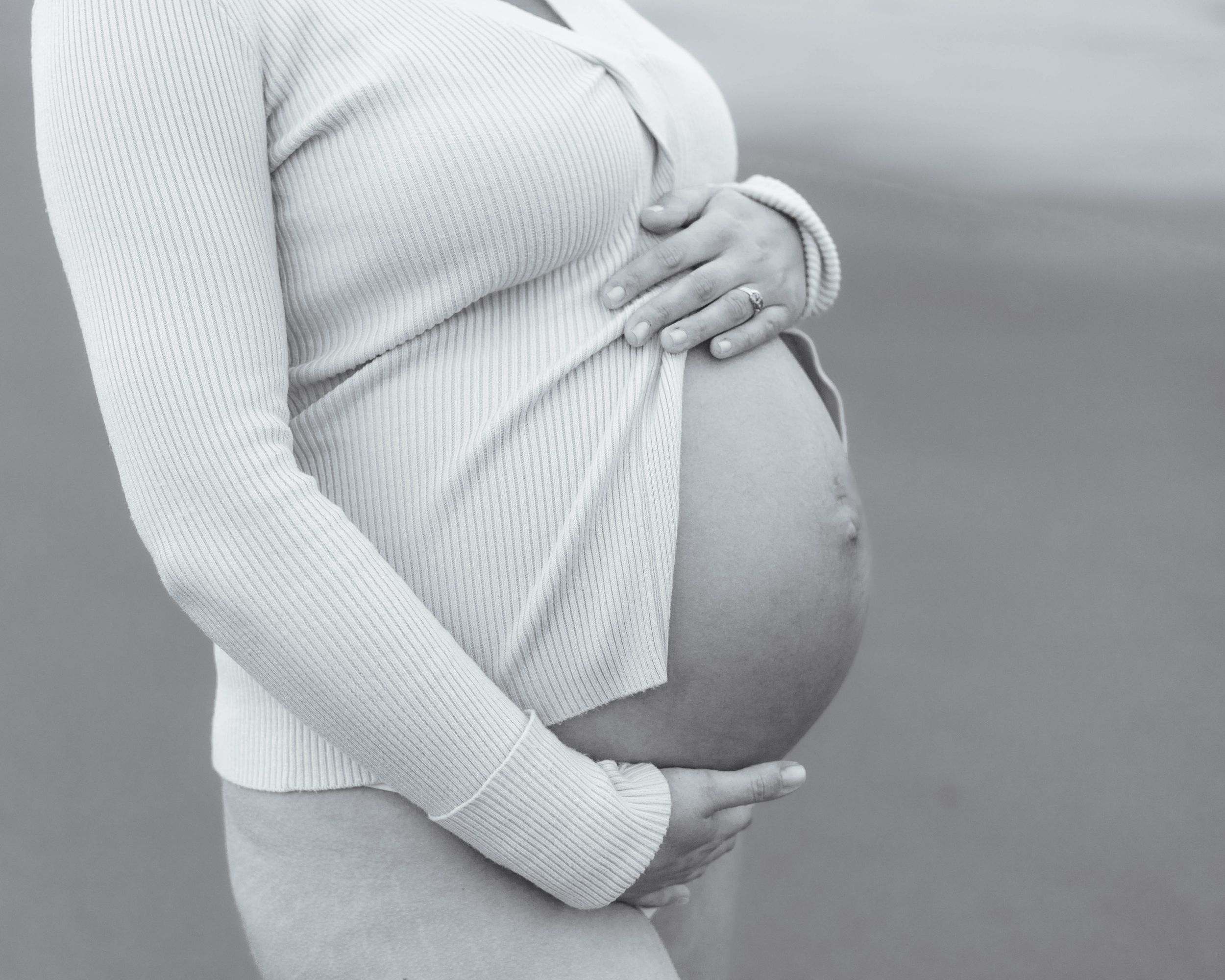 Hands cradling a pregnant bump in soft cream knitwear