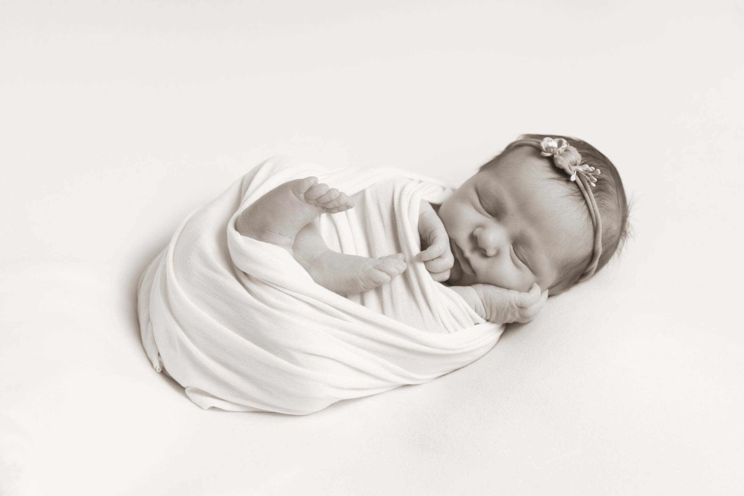 Newborn baby swaddled in a soft white wrap, fast asleep