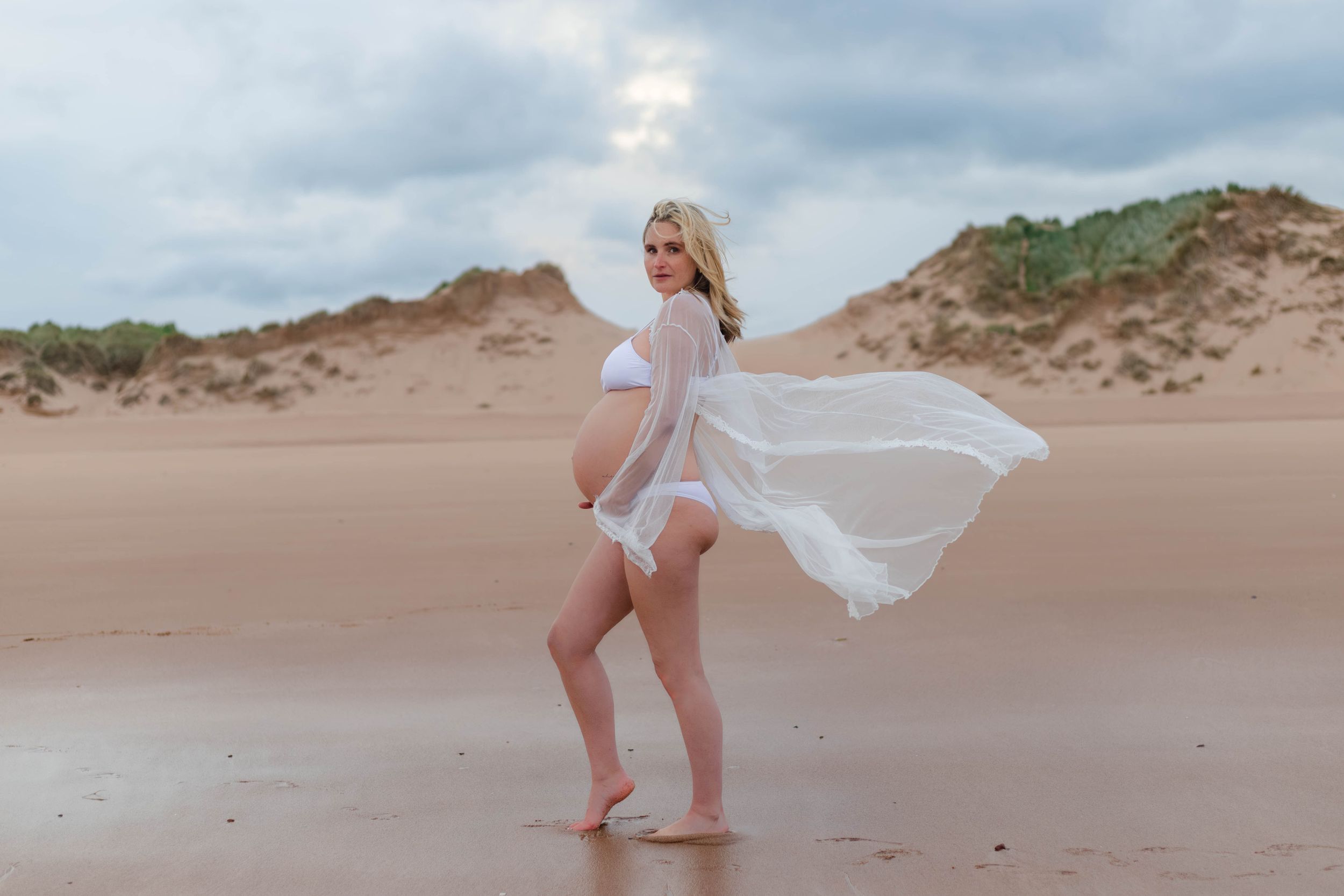 Expectant mother in a flowing white dress on the dunes at Balmedie beach