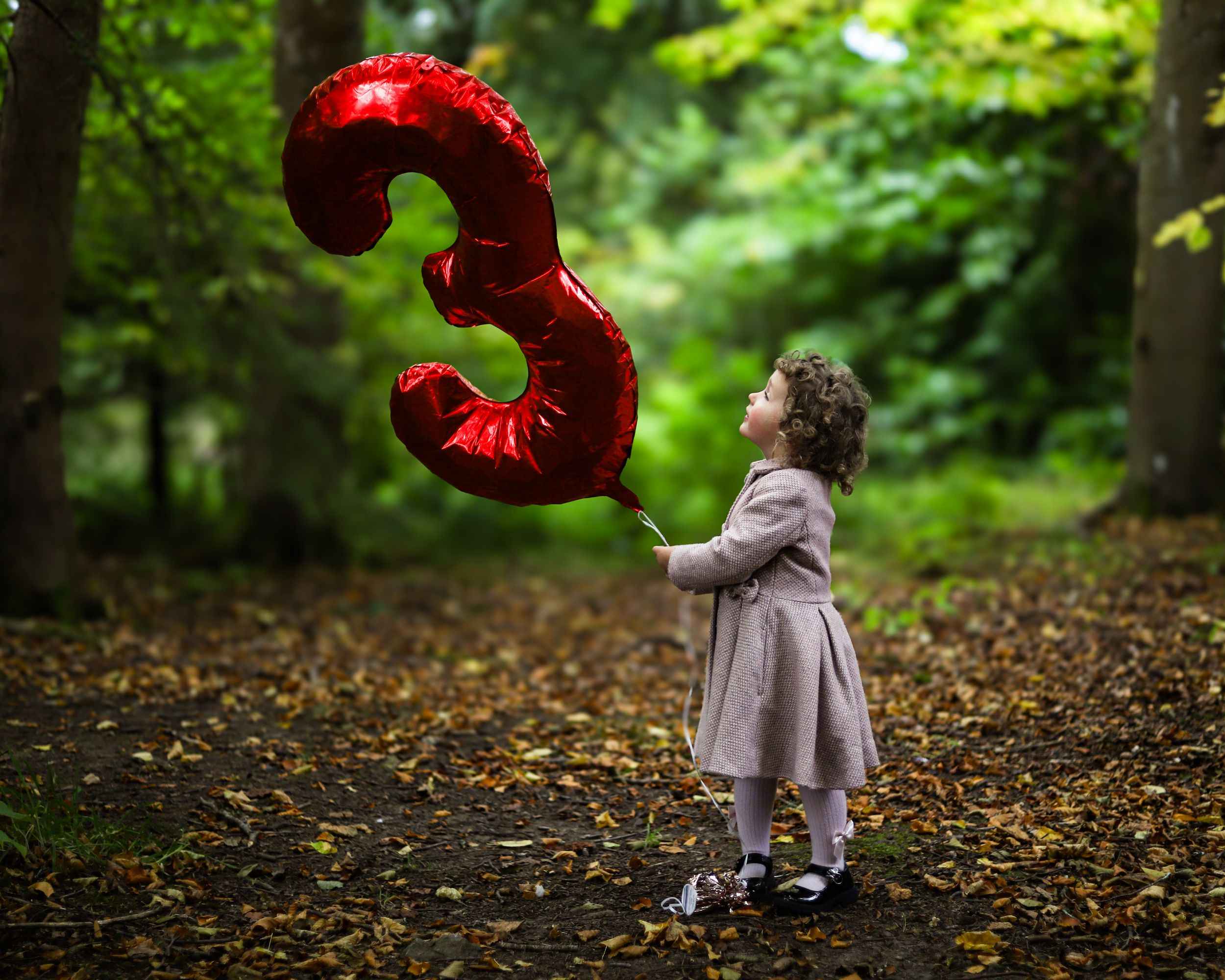Little girl holding a giant red number three balloon in autumn woodland
