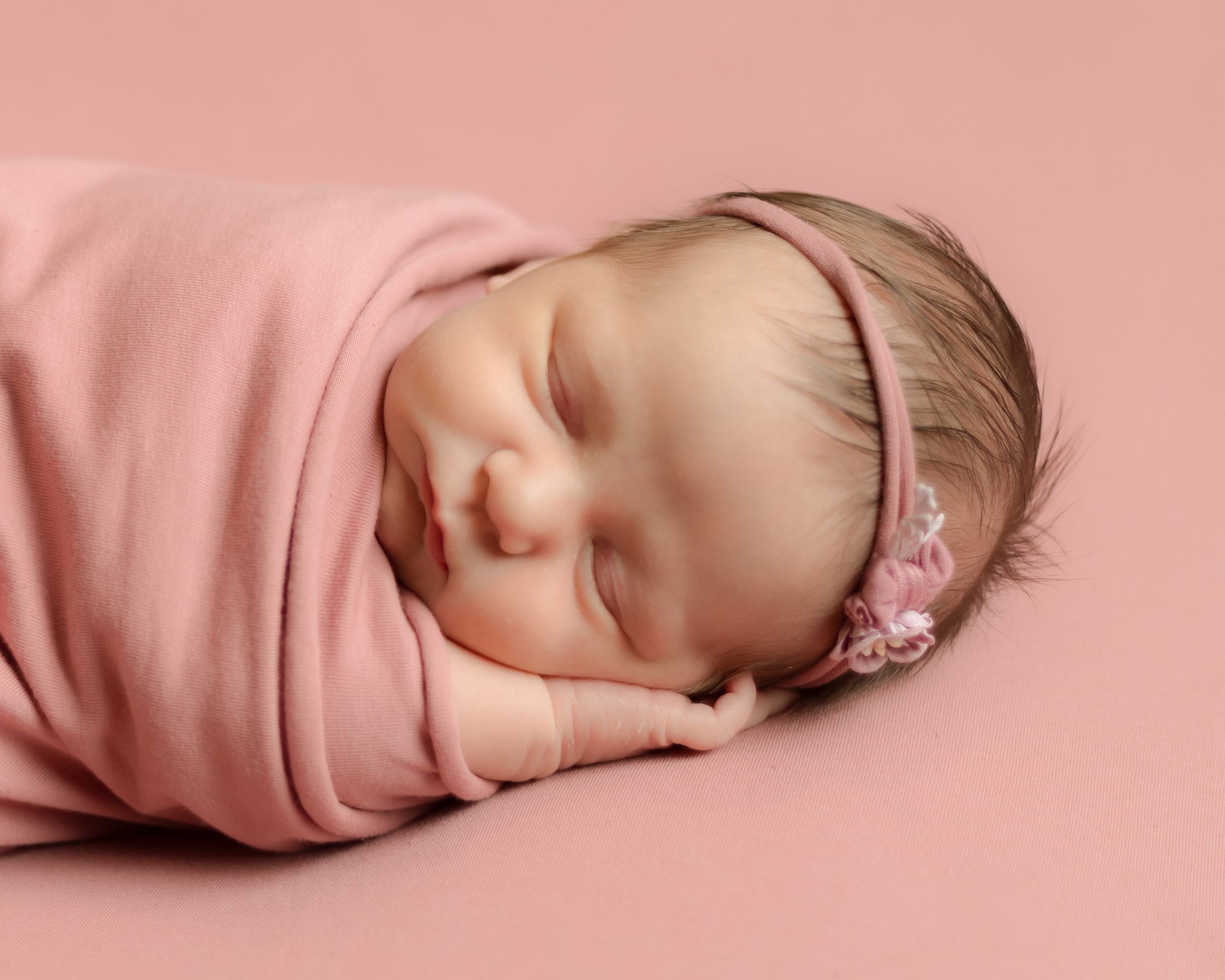 Sleeping newborn wrapped in a blush blanket with a flower headband